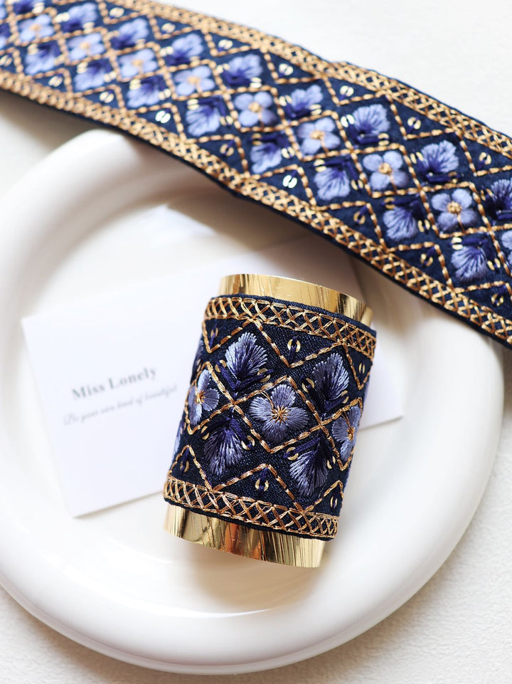 This elegant hair wrap showcases a soothing blue base adorned with intricate lilac and gold embroidery. The delicate floral design brings a touch of serenity and grace to your look.