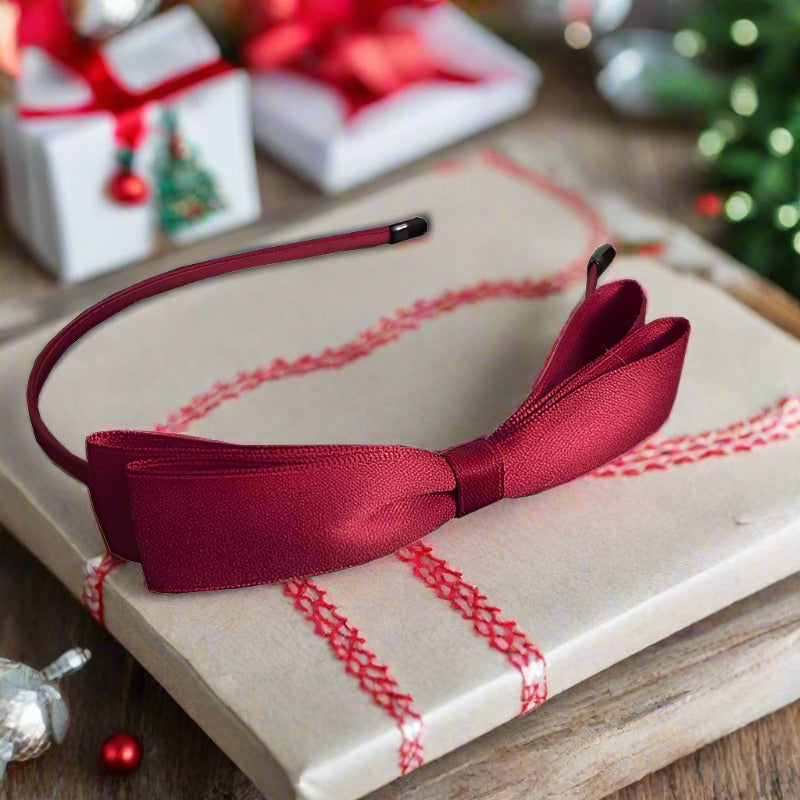 A beautiful red headband adorned with a large satin double-layer bow, perfect for adding a touch of elegance to any girl's outfit. The bow measures approximately 14 cm, making it a standout accessory for special occasions such as birthdays and the holiday season like Christmas and New Year. This close-up showcases the intricate design of the large red satin bow on the headband, highlighting its luxurious sheen and sophisticated style. Ideal for festive events and elegant looks.