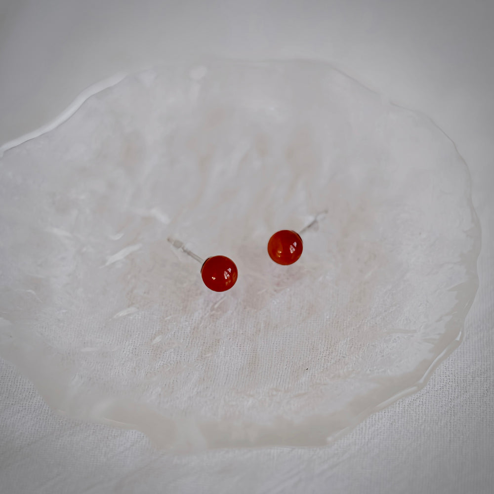 A detailed shot of a pair of 6mm red onyx stud earrings, highlighting their polished surface and vibrant hue.