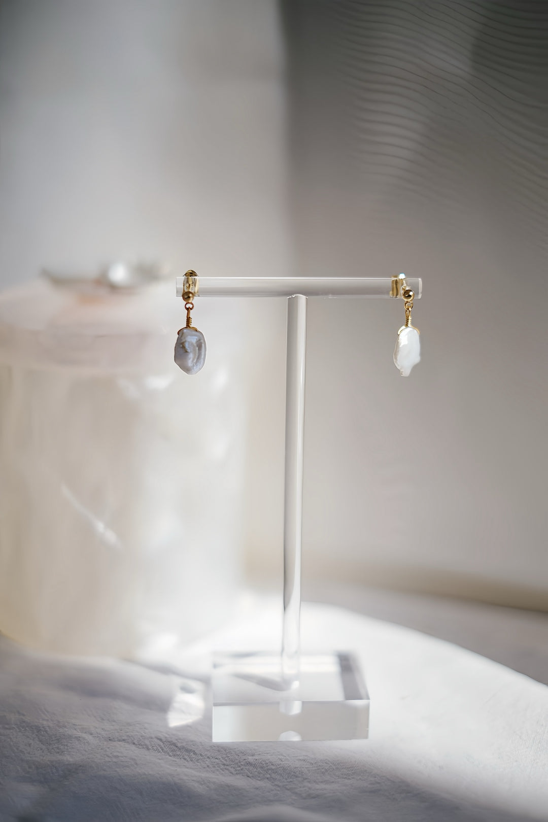 The Luminous Coin Pearl Dangle Earrings placed on a minimalist, neutral backdrop, allowing the pearls' natural luster and the gold-filled accents to take center stage.