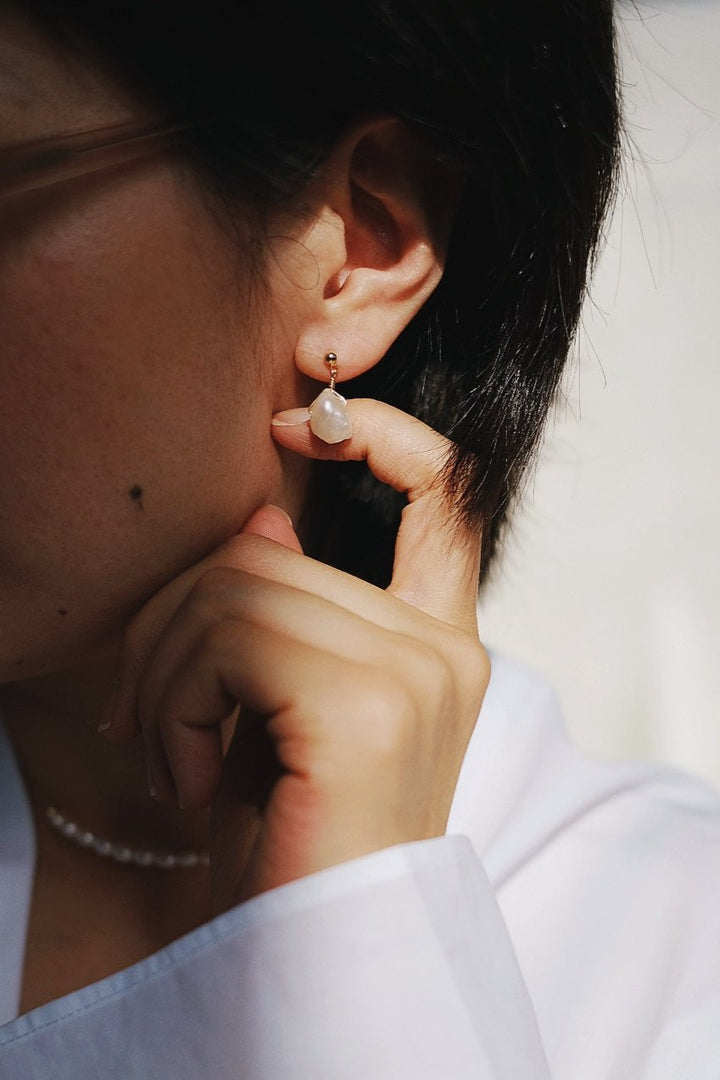 A model gracefully displays the Luminous Coin Pearl Dangle Earrings, with the flat, shimmering coin pearls gently swaying and catching the light against her ear.