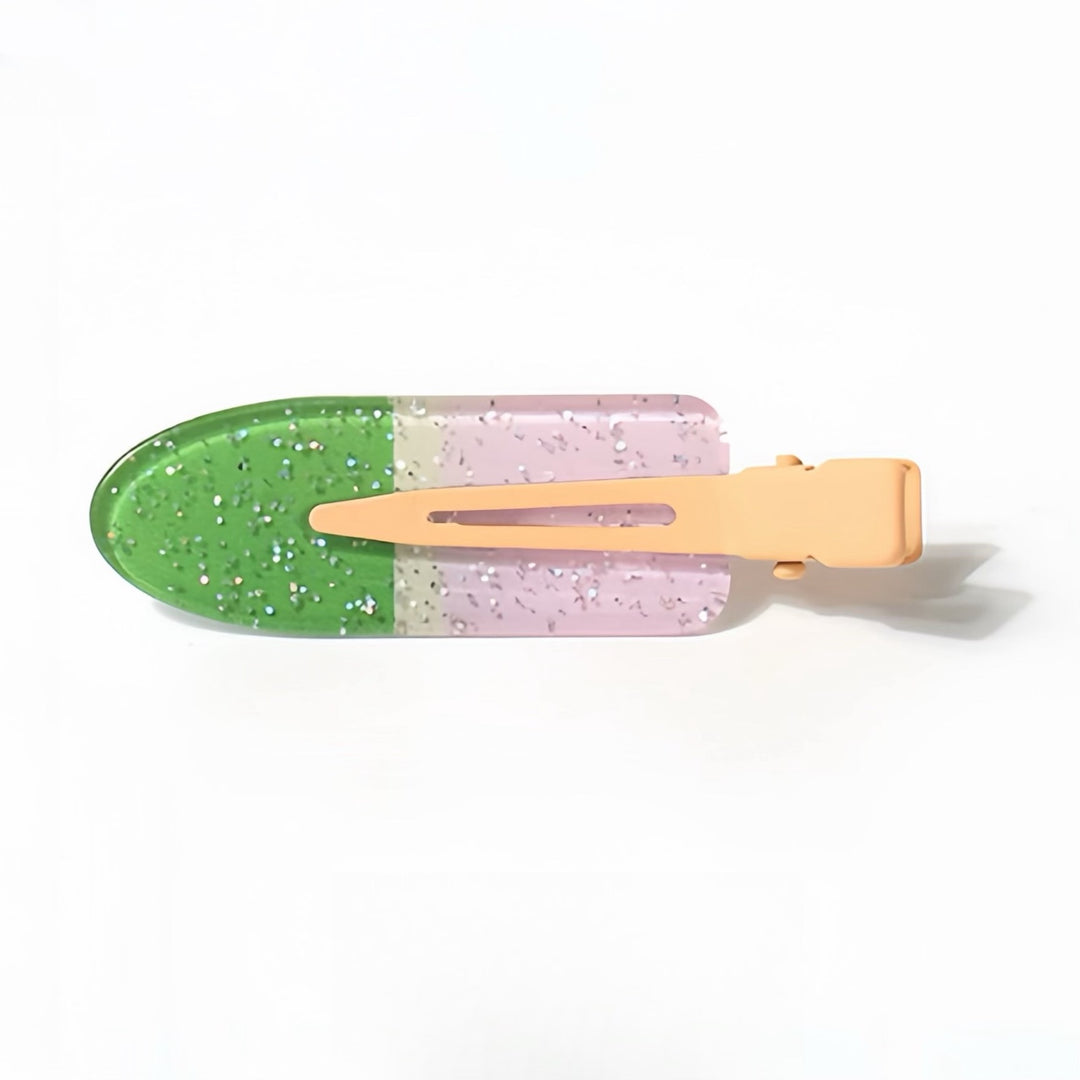 The Green and Lilac Resin Hair Clip with Silver Glitter features a vibrant green tip that transitions into a lilac body sprinkled with silver glitter. The 6 cm clip has a light orange handle, creating a cheerful and glittery accessory that shines in any light.