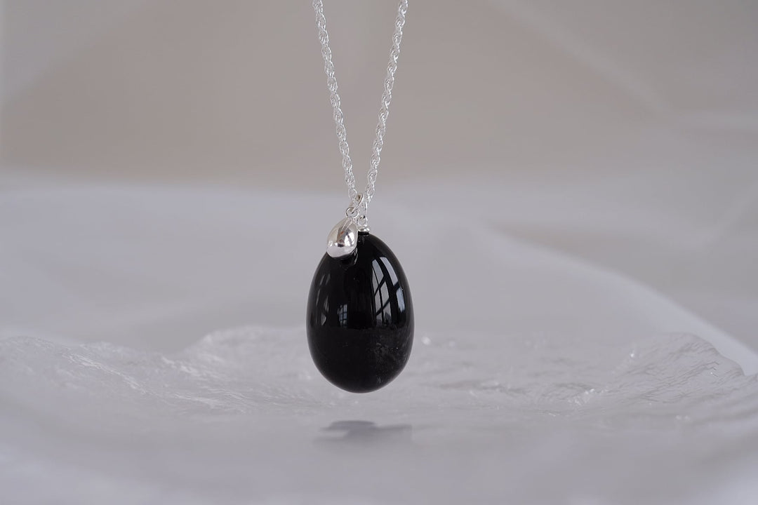 A close-up of the large obsidian pendant on the Teardrop necklace, highlighting the deep, glossy black of the gemstone against a white backdrop.