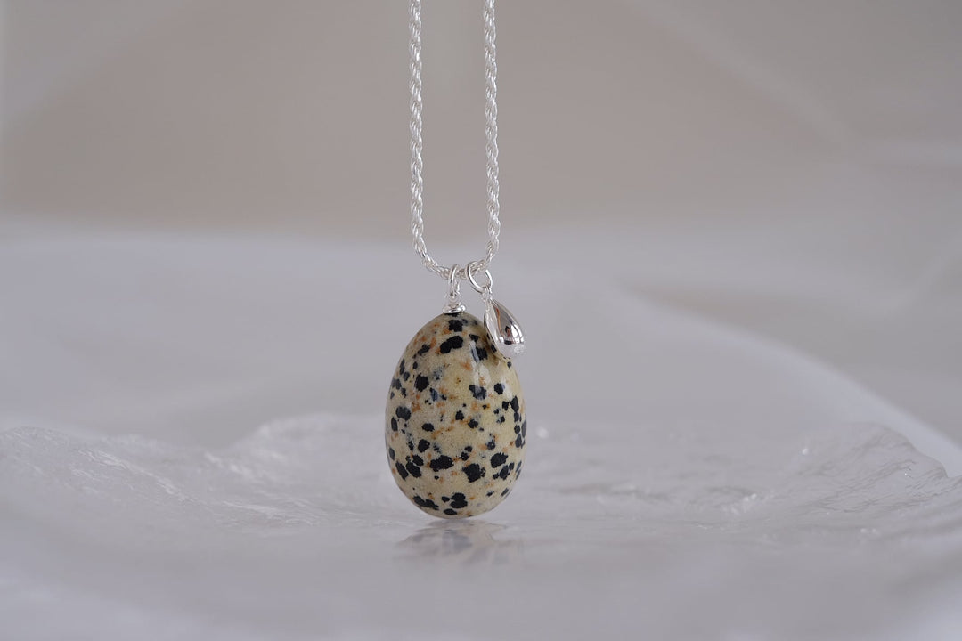 The distinctive Dalmatian jasper gemstone is characterized by its cream or beige base with black or brown spots. Combined with its teardrop shape, the pendant reminds one of a bird's egg.