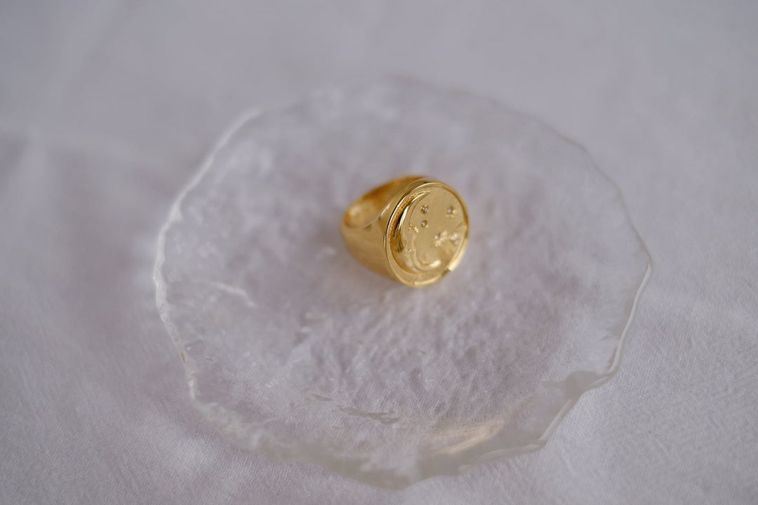 The Moon signet ring displayed on a white stand, emphasizing its elegant design and luxurious gold plating.