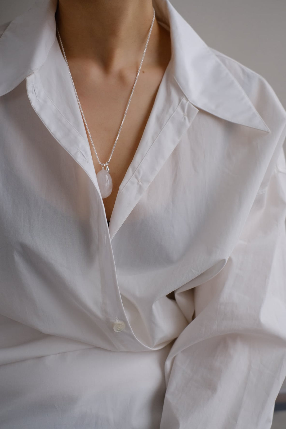 The large white crystal pendant on a Teardrop necklace, worn with a minimalistic outfit to highlight the gemstone's pure and elegant design.