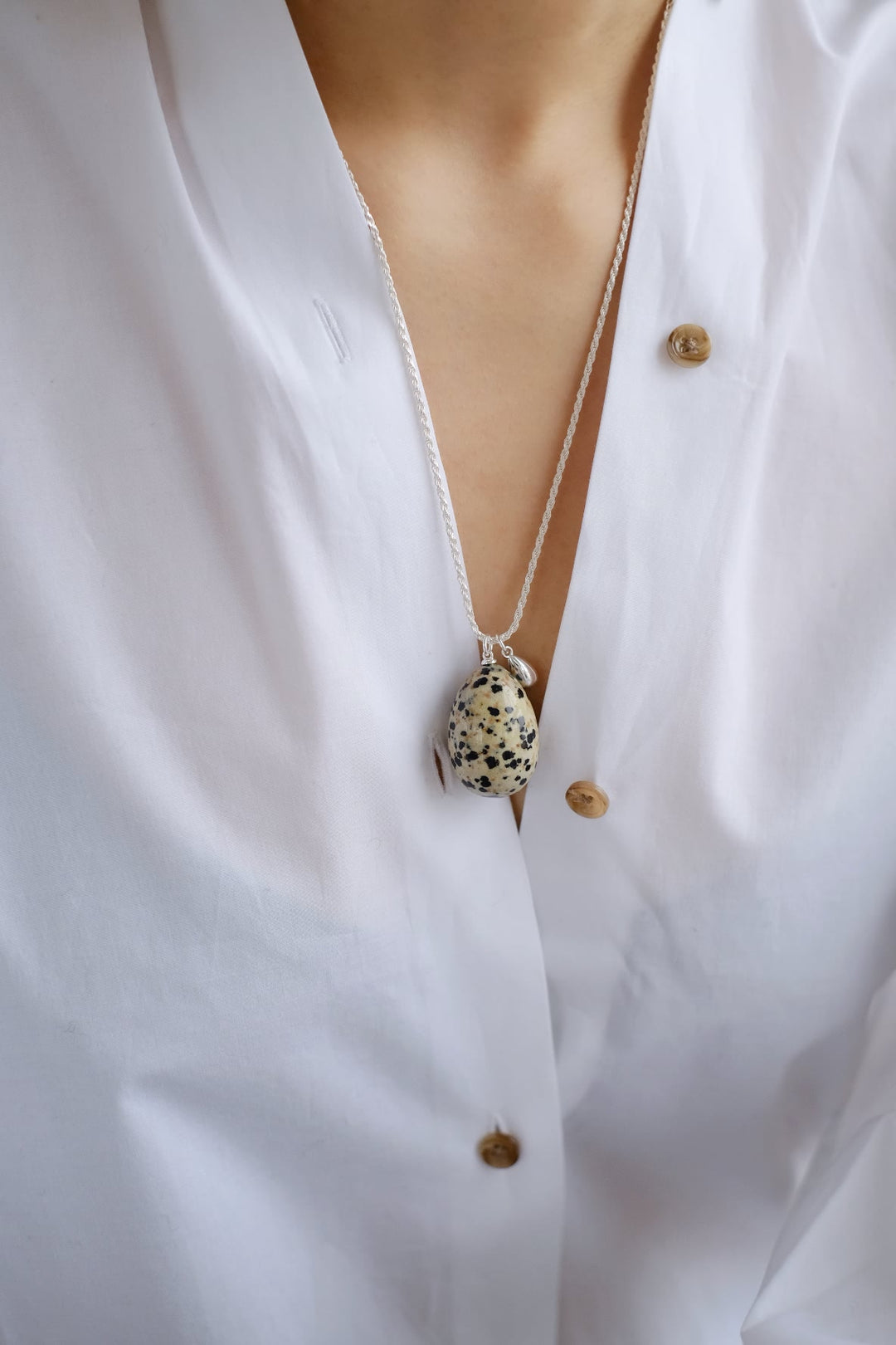 The large dalmatian jasper pendant necklace worn over a white shirt, showcasing how the unique gemstone stands out as a statement piece.