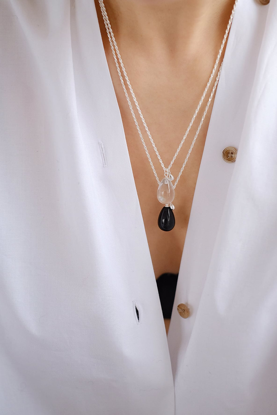 A pair of Teardrop necklaces with the small pendants, showcasing their rich, black luster of obsidian and the pure clarity of white crystal, and how they complement each other when layered.