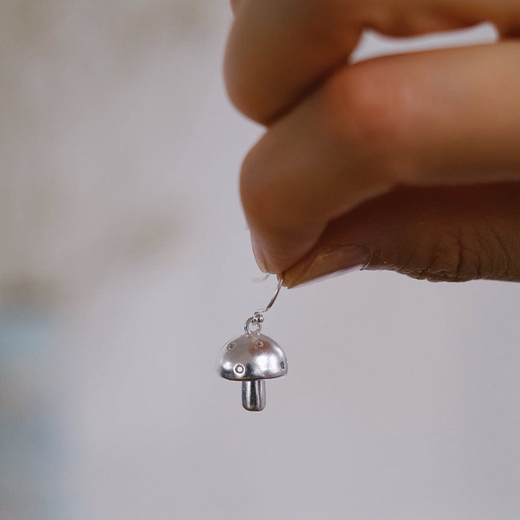 Close-up of a sterling silver mushroom earring held by a hand, showcasing its detailed design.