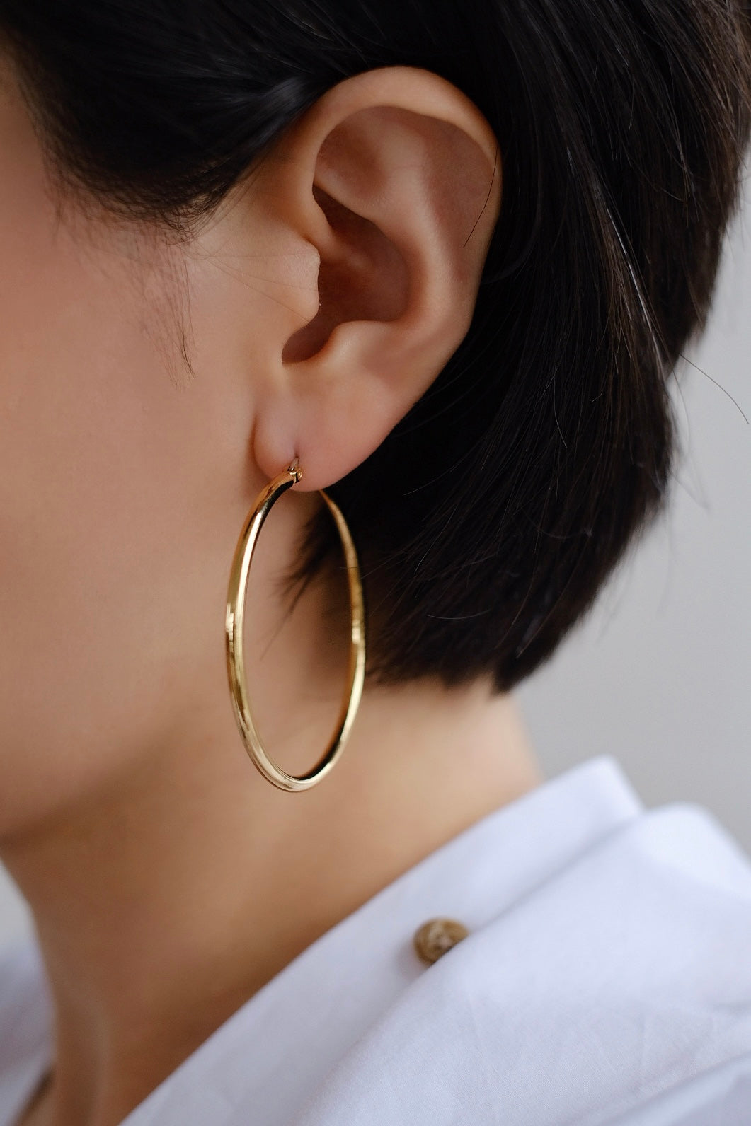 A side profile of a model wearing these golden hoops, demonstrating their perfect size and radiant appearance against the skin.