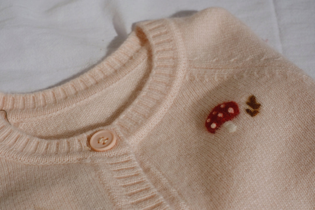 Detailed embroidery of red mushrooms adds a whimsical touch to the front of the cardigan, perfect for sparking imagination in little ones.