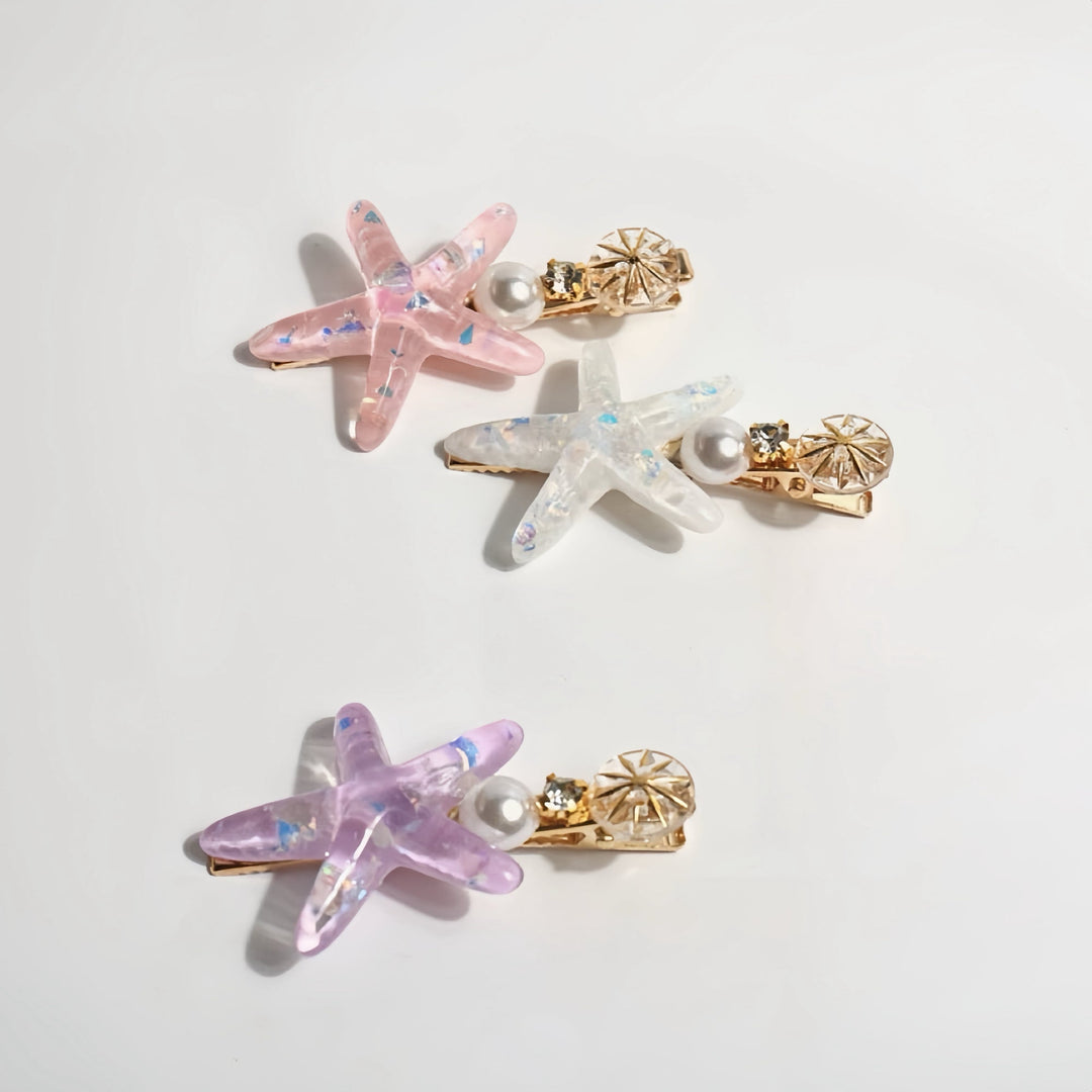 Three starfish-shaped hair clips in pastel colors—pink, white, and purple—arranged on a white background.