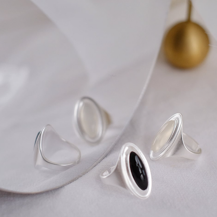 The Goddess silver open ring set against a mirror, showcasing its dual gemstone design: a choice between translucent white agate or deep black onyx.