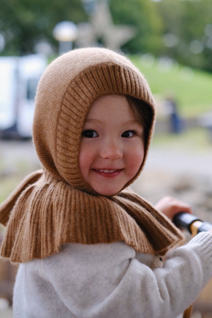 A cozy caramel-colored hat sits snugly on a young child’s head, showcasing its soft, warm texture.