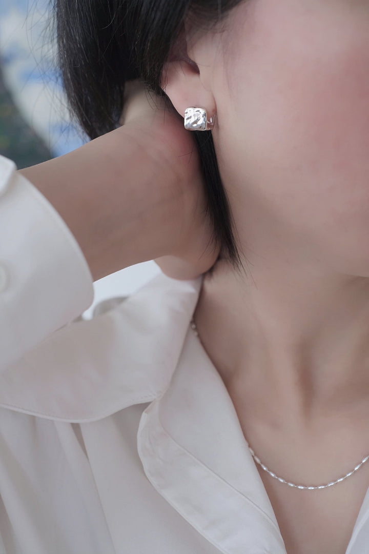 Side view of the earring on the model's ear, emphasizing the unique square design and polished surface.