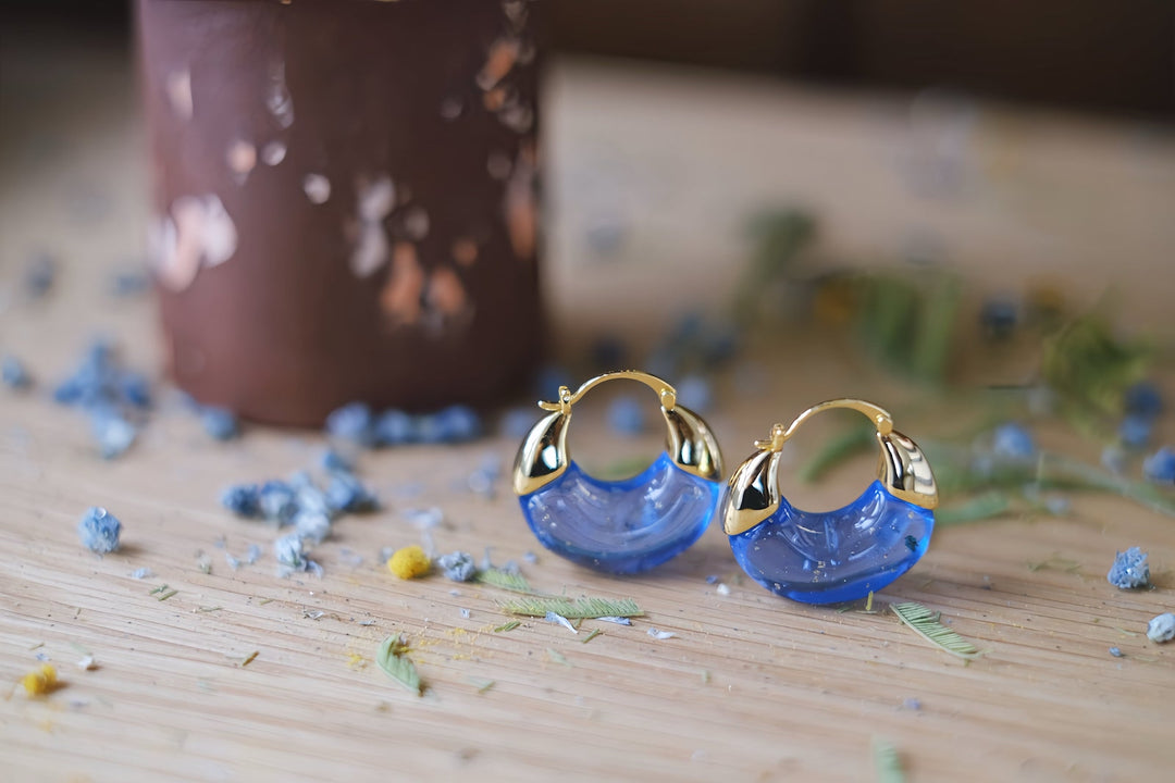 The blend of vibrant blue and shimmering gold captures the essence of a serene ocean under a starlit night, making these earrings a unique and captivating addition to any jewelry collection.