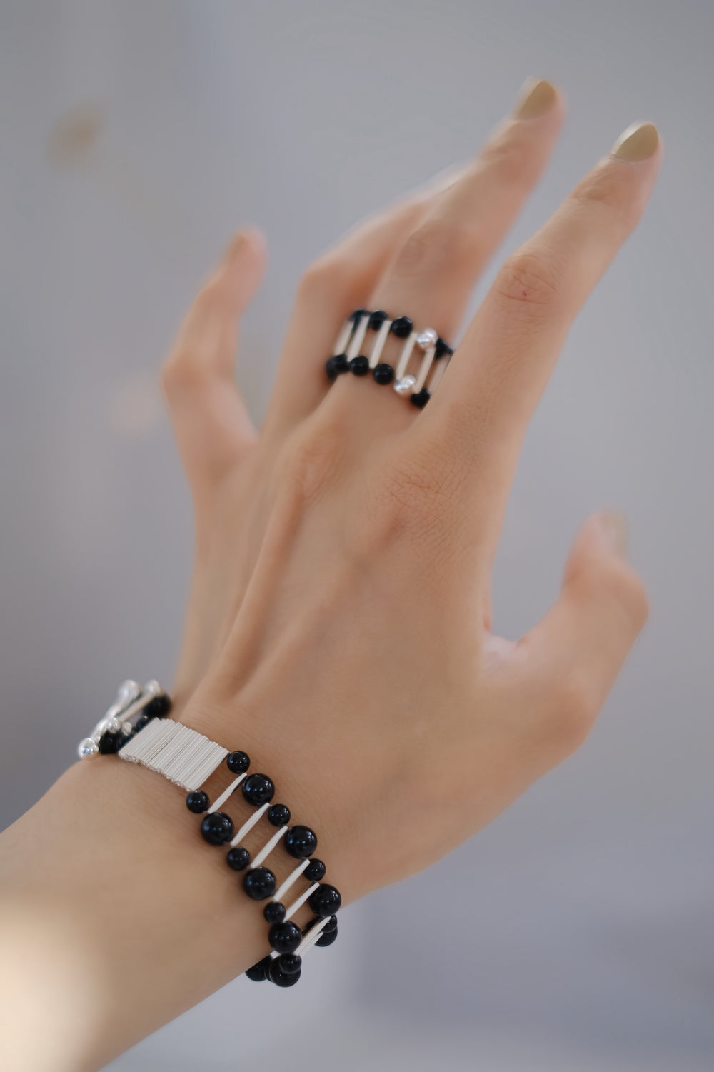 A close-up of a woman's hand wearing the Midnight Whisper bracelet and ring set, featuring sterling silver and black onyx beads. The bracelet's distinctive armor-like clasp symbolizes resilience, while the elastic ring offers a perfect fit. Ideal for those seeking a blend of vintage elegance and modern sophistication.