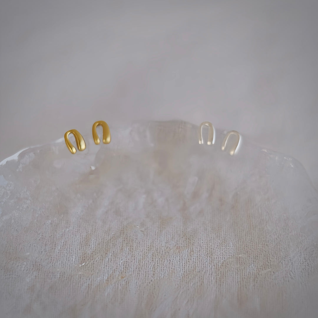 A close-up shot of two pairs of Mini Horseshoe earrings in sterling silver and gold-plated sterling silver, highlighting their intricate horseshoe shape and smooth finish.