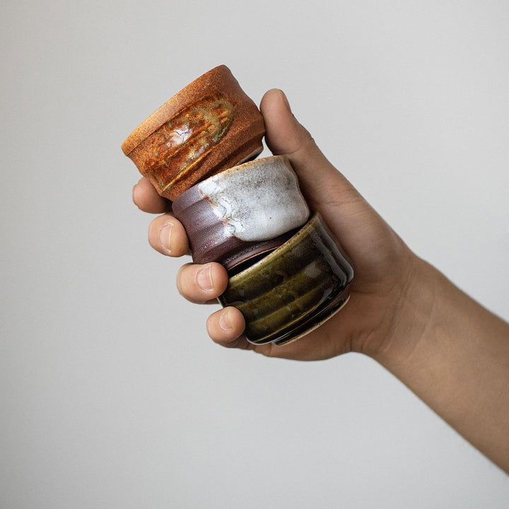 A person holding three of the Minoyaki cups in one hand, demonstrating their compact 60ml size. This image highlights the practical, yet elegant design, perfect for tea tasting or espresso drinks.