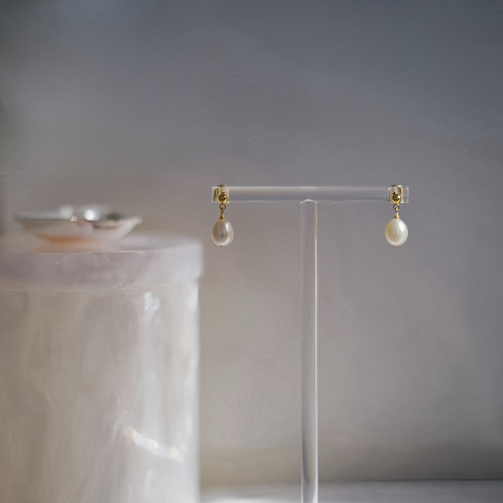 The Petite Pearl Drop Earrings resting on a earrings stand, emphasizing their elegant and lightweight design.