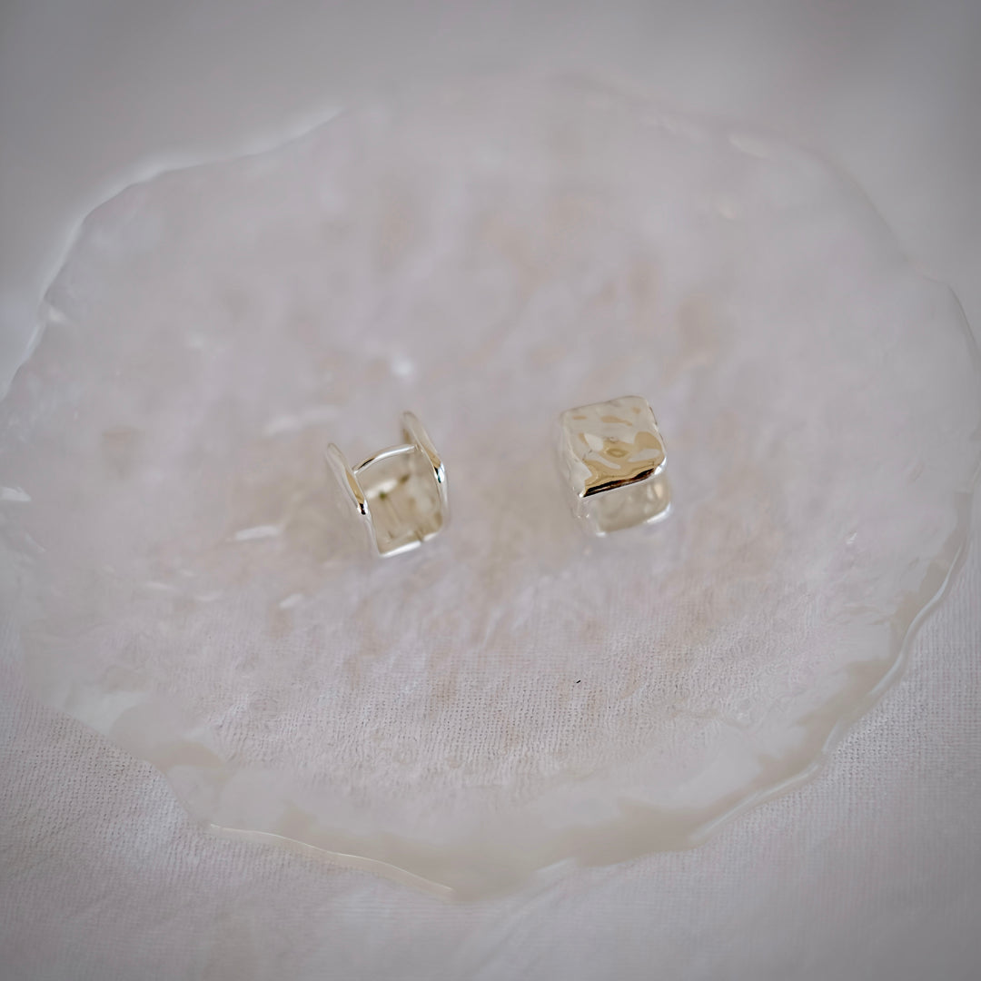 A close-up shot of the Cube silver huggie earrings, showcasing their slim profile and lightweight nature.