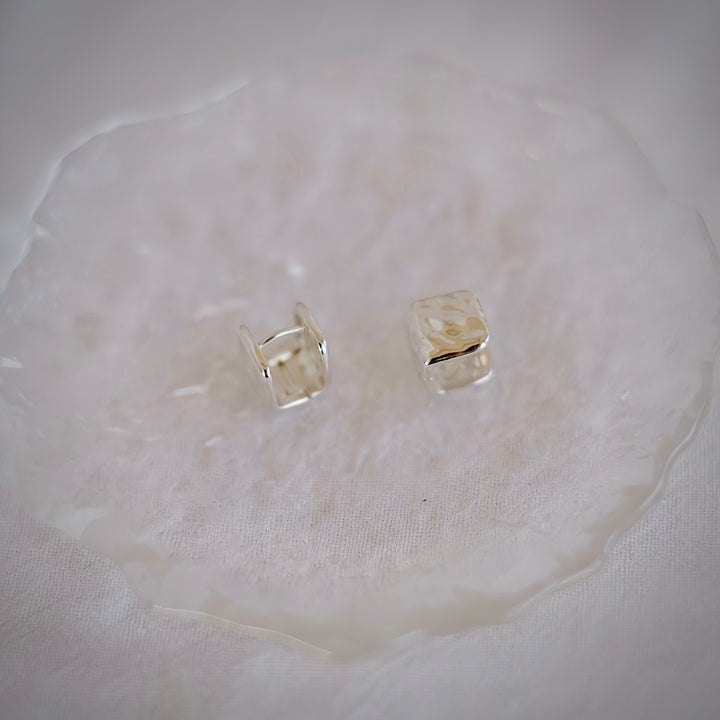 A close-up shot of the Cube silver huggie earrings, showcasing their slim profile and lightweight nature.