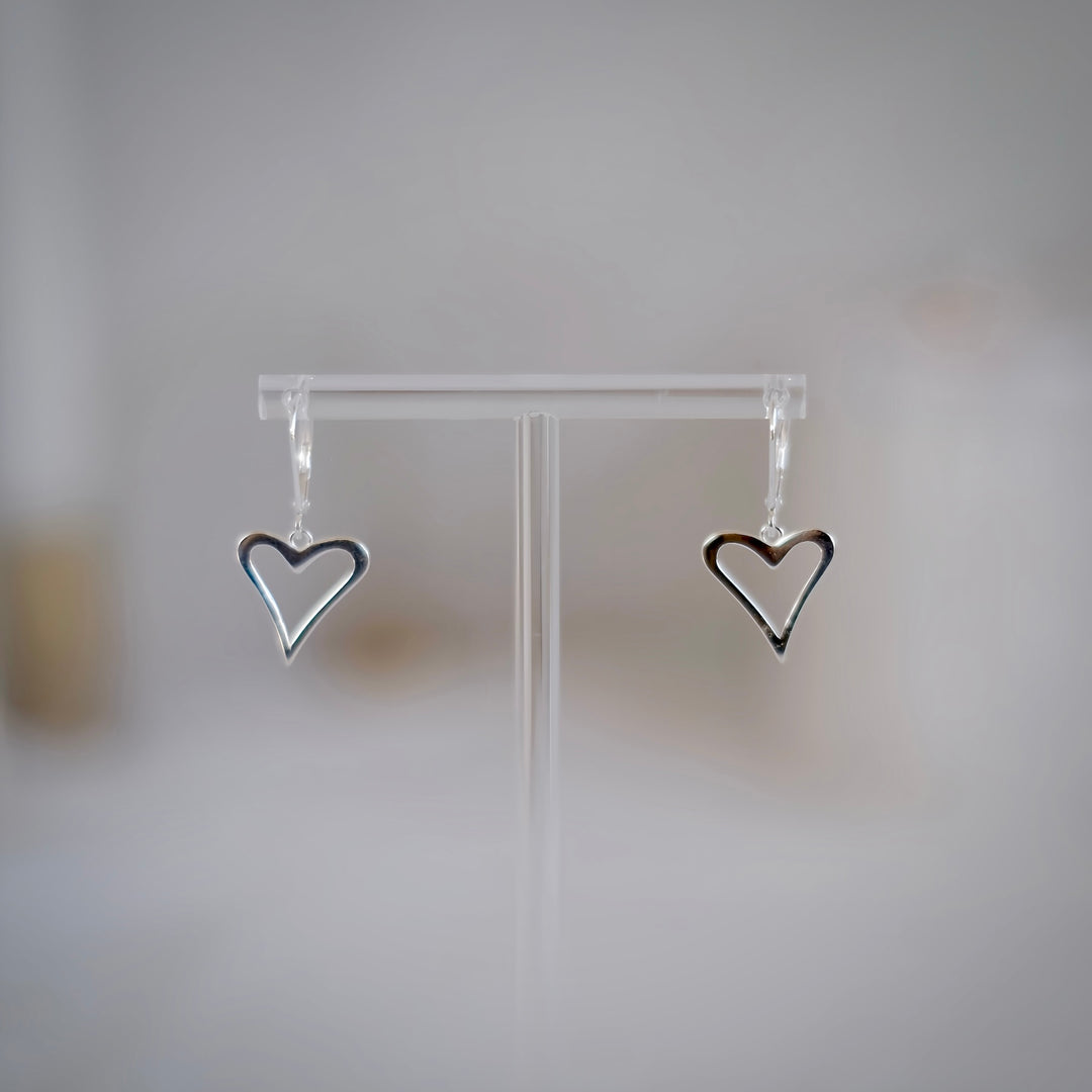 A pair of sterling silver heart-shaped earrings draping elegantly on a earring stand, showcasing their shiny, polished finish and delicate design.