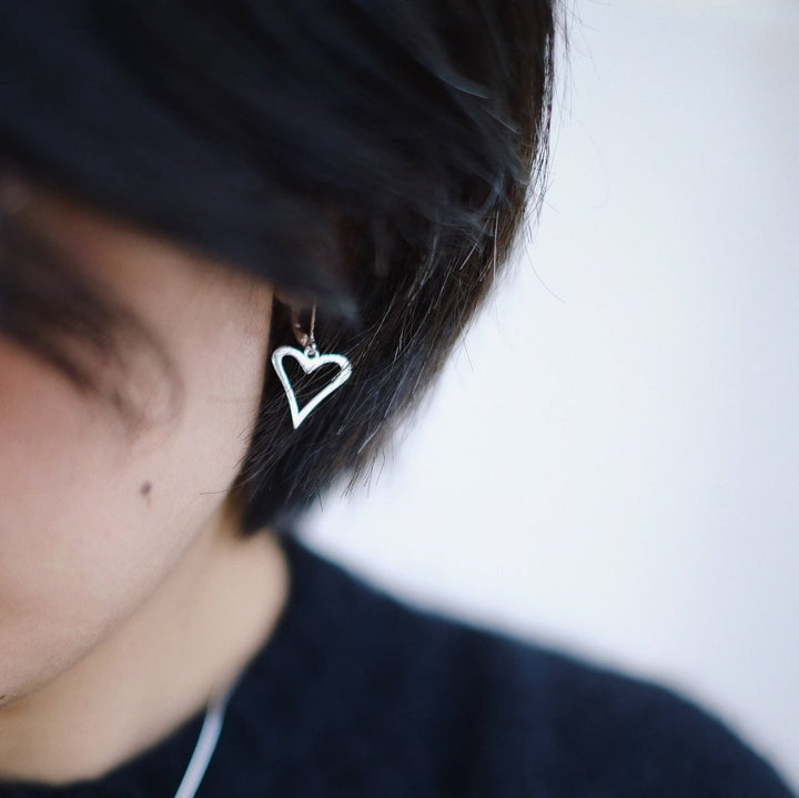 A model wearing the heart-shaped earrings, the delicate silver hearts dangling playfully and adding a cute, charming touch to her look.