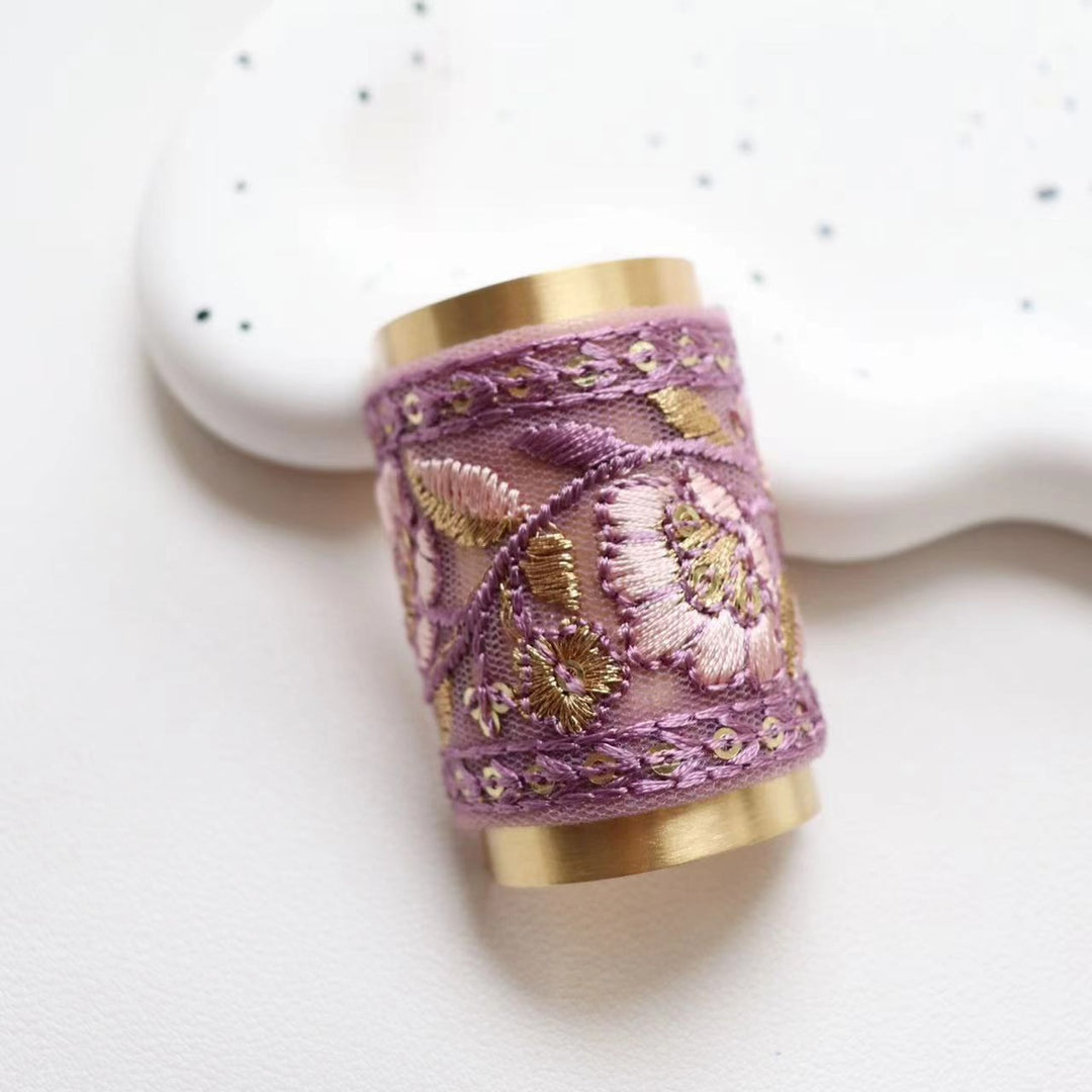 The Lilac Whisper hair wrap presents a lovely purple fabric with intricate floral embroidery in gold and white. This unique and eye-catching design brings a regal and sophisticated touch to your hairstyle.